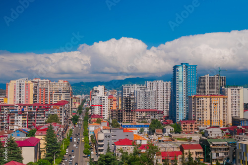 View of Chavchavadze street of Batumi, Georgia with typical residential buildings, road with moving cars, daylight. White clouds in the blue sky are over the mountains. Cityscape and urban concept