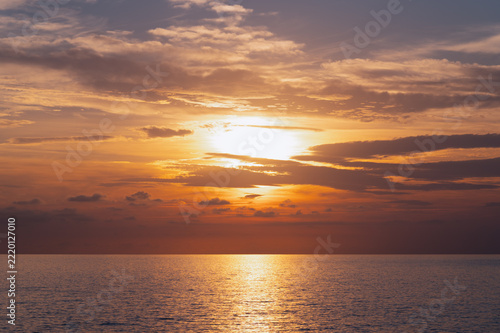 Sunset sun glowing over calm ocean expanse with clouded sky