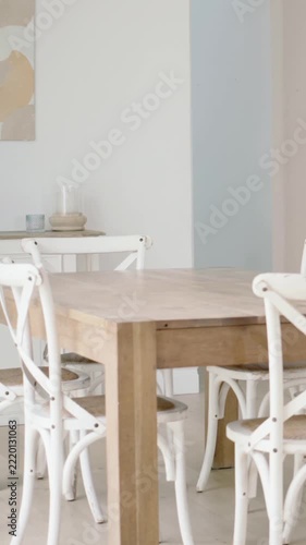 Vertical video: Panning camera left revealing wood table with white chairs in home and wall niche