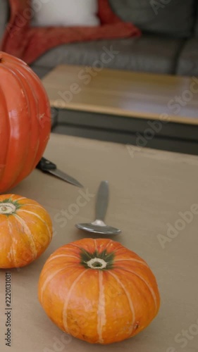 Vertical video: Shifting camera revealing pumpkin trio on brown paper at home, showing spoon, knife