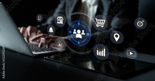 Business professional working on laptop with digital icons representing online marketing, data analysis, and e-commerce concepts in a dark environment. Glyphic.