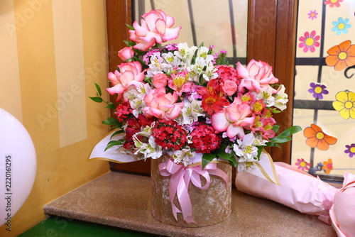 Beautiful floral arrangement of pink roses and alstroemerias in a decorative gift box standing on a window sill.The colorful bouquet creates a festive atmosphere for celebrations and special occasions