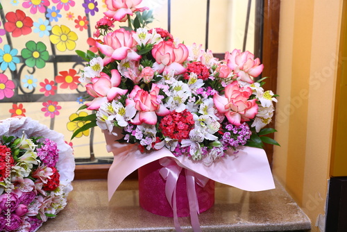 Beautiful floral arrangement of pink roses and alstroemerias in a decorative gift box standing on a window sill.The colorful bouquet creates a festive atmosphere for celebrations and special occasions