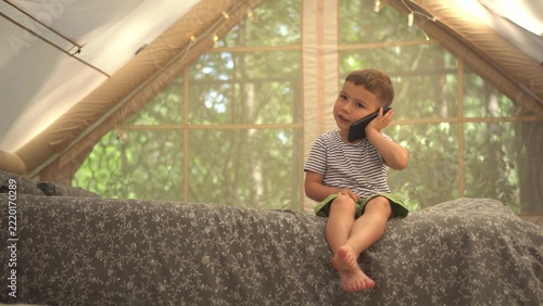 Little Boy Relaxing in Inflatable Play Tent on Bed While Talking on Smartphone