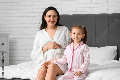 Maternity and family bonding, pregnant mother and young daughter sitting on b...