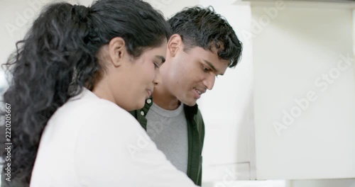 Diverse couple starting meal prep, smiling and stirring peppers with spatula in frying pan on stove