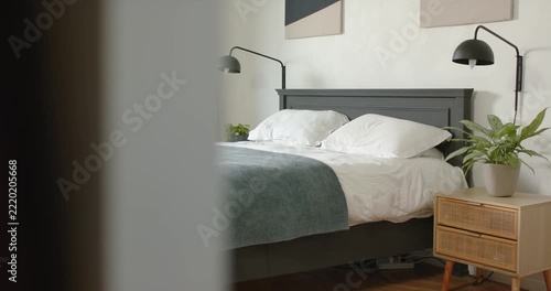 Camera is panning right from doorway revealing bed with dark gray headboard, teal throw, nightstand