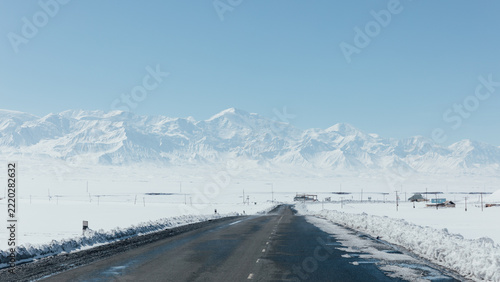 Obraz na plátně Straight asphalt highway crossing a vast snow covered plain toward huge snowy mo