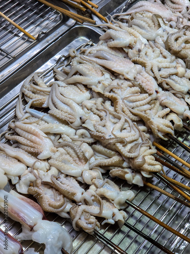 A dense pile of small pale octopus tentacles skewered on wooden sticks, heaped inside a stainless steel tray.