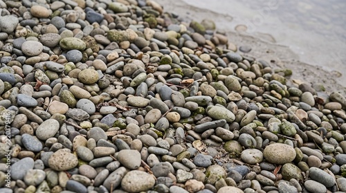 Close up of diverse natural pebbles on sandy beach shoreline