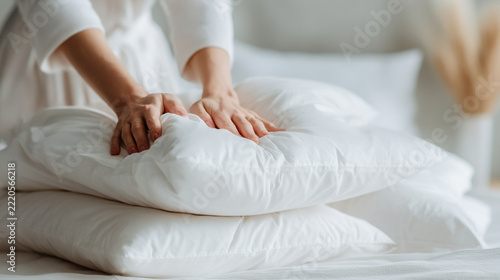 A close-up shot shows a person's hands fluffing a stack of clean, white pillows, suggesting comfort, rest, and a tidy bedroom. HD Quality, Stock Image