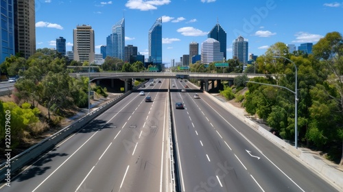Aerial View of Urban Highway with Cars and Modern City Skyline Under Bright Blue Sky