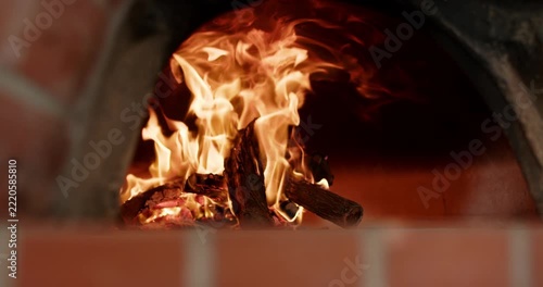 Log stack is burning after ignition, flames are rising, curling in brick oven to heat interior