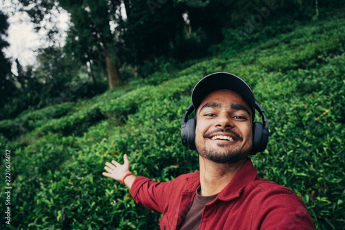 Canvas Print Indian man taking a selfie at a scenic tea garden surrounded by lush green tea bushes and rolling hills
