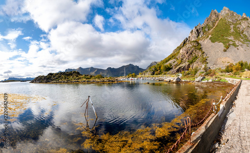 Rocky bay near Valberg on Vestvågøya with calm water, rugged mountains,small harbor, autumn vegetation and blue sky.