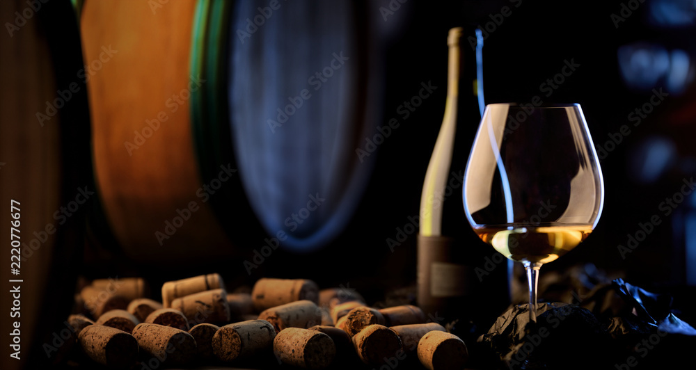 Fototapeta premium Golden white wine in elegant glass on dark background. Wine cellar of vinery with barrel and corks.