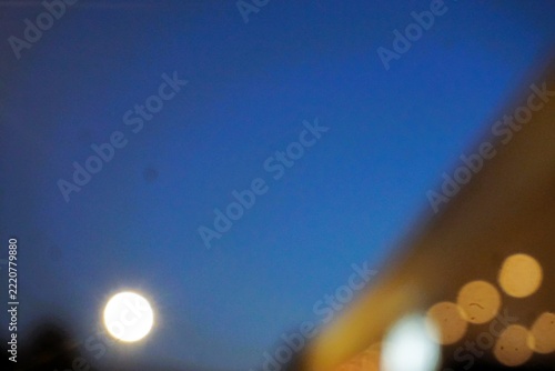 Abstraktes Motiv mit goldbraunem großen beleuchtetem Gebäude mit Flachdach mit goldgelben runden Lichtern vor dunkelblauem Himmel bei Vollmond in der Nacht im Herbst