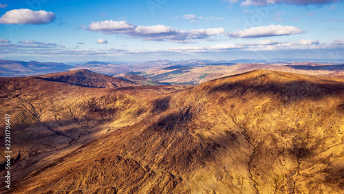 Rugged mountainous landscape featuring rolling hills and vast golden plains under a bright sunny sky during late afternoon.