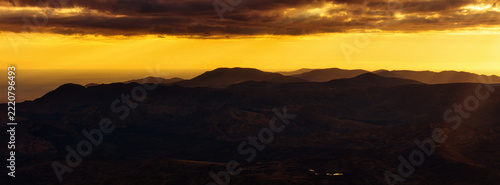 Golden clouds glow brightly above the dark ridges of the Irish mountains as the day ends and evening light covers the landscape.