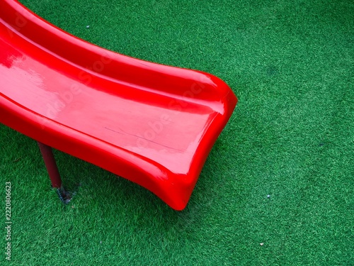 Vibrant Red Plastic Playground Slide on Synthetic Green Grass Surface