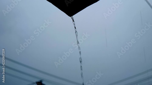 rainwater pouring from roof gutter during heavy rain video screenshot, rain drops streaming down from house roof edge against overcast sky, close up of water pouring from roof edge during rainy weathe