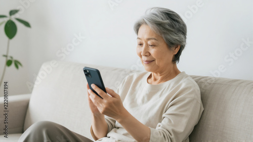 Smiling Senior Japanese Woman Sitting on Sofa Using Smartphone at Home