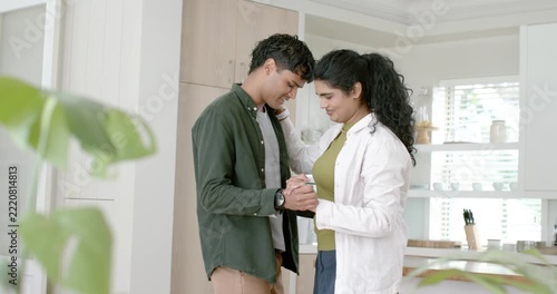 Indian couple holding hands, leaning foreheads, embracing and swaying in kitchen showing love
