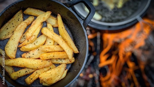 Campfire Fries: Rustic potato wedges seasoned with herbs, cooked to golden perfection in a cast-iron pan over an open campfire. A hearty and delicious outdoor meal, perfect for any adventure.