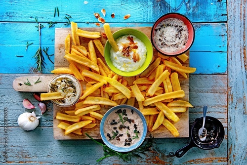 French Fries Feast: A delectable assortment of golden french fries is served with an array of creamy dips on a rustic wooden board, inviting a shared culinary experience.