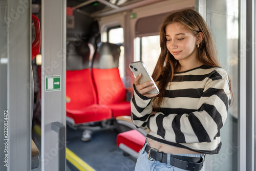 Young woman checks her mobile phone while standing in train carriage during daylight hours