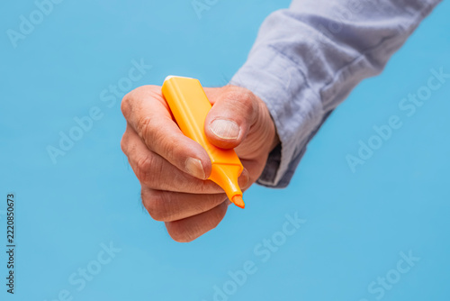 Hand holding an orange highlighter against a vibrant blue background. This image is perfect for office, education, business planning, and creative project concepts.