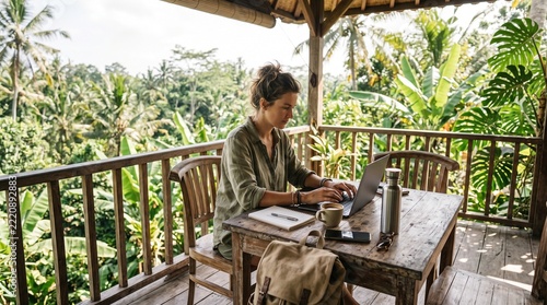 Young woman working on a laptop at a wooden table in a tropical setting. Remote Work & Digital Nomad  