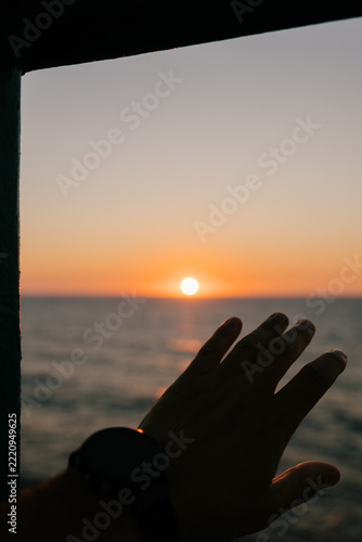 POV of a hand raised to admire an ocean sunset, evoking freedom.