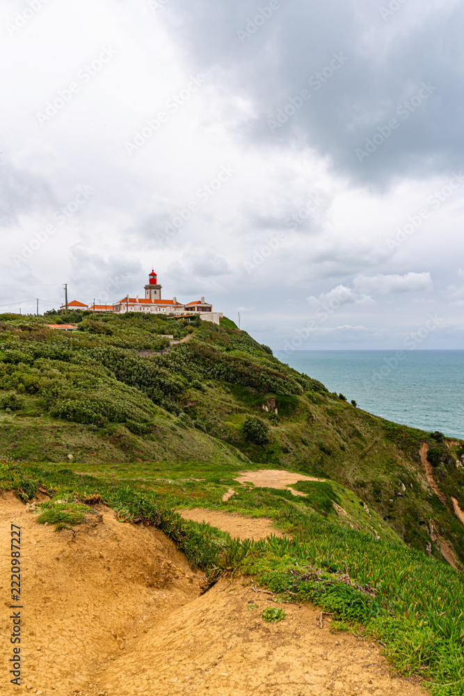 Fototapeta premium Cabo da Roca dramatic coastal cliff overlooking Atlantic Ocean in Portugal. Scenic westernmost point of Europe with rugged landscape, ocean waves and natural coastline.