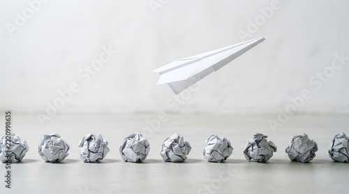 White paper airplane flying above a row of crumpled paper balls on gray background for leadership and success concept