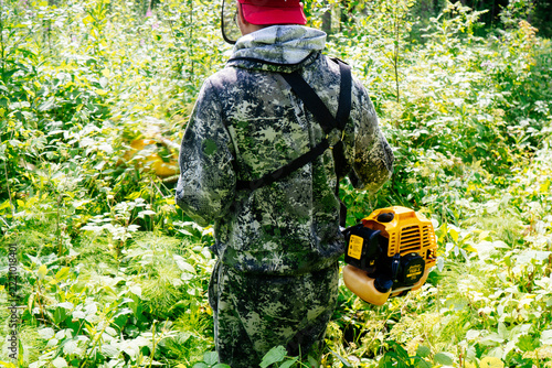 a man in work clothes and a protective mask mows grass in the wilderness with the power of a gasoline trimmer