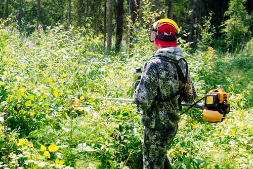 a man in work clothes and a protective mask mows grass in the wilderness with the power of a gasoline trimmer