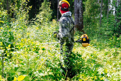 a man in work clothes and a protective mask mows grass in the wilderness with the power of a gasoline trimmer