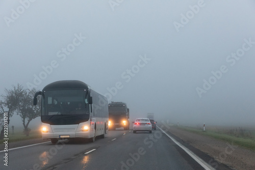 A bus, a truck and cars on a country road in the fog. Poor visibility on the road.