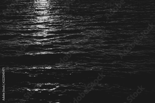 Dark water with streak of light from a distance. Gentle waves highlighted by the light source. 