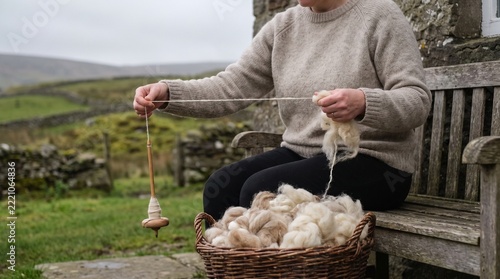 Woman letting a drop spindle twirl as she draws a fine thread of cream fleece between her fingers on a stone cottage porch