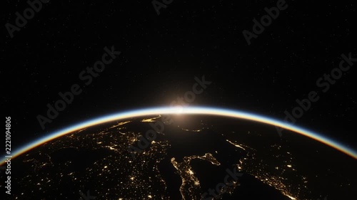 Sunrise over Earth from space, sun rising above glowing atmosphere as city lights fade into daylight
