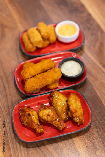 Roasted grilled chicken legs or baked chicken wings new orleans and barbecue or bbq with fish and chip and fried cheese dip sauce on wooden table by top view for protein food to lunch in restaurant