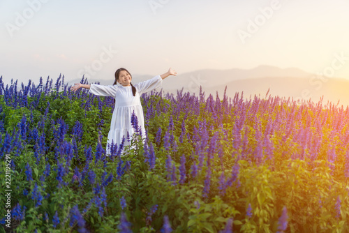 Asian child in flower field or kid girl standing on beauty of many fresh flowers to happy smile on beautiful blue in nature garden on travel and mountain sky view with warm sunlight at flower garden