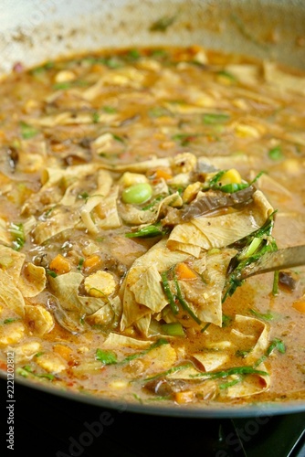 Close-up high angle shot of cooking Bubur Pedas, a traditional rice porridge dish popular in Sarawak, Malaysia, and West Kalimantan, Indonesia. The savory dish is enriched with mixed vegetables, herbs