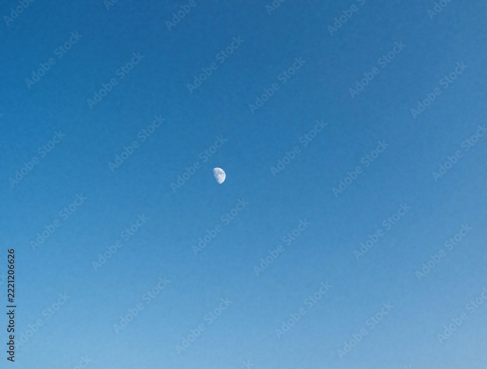 Fototapeta premium Small crescent moon hangs in clear blue sky. Minimalist bright day sky with tiny lunar phase. Vast empty space for copy. Calm atmosphere, serene nature background. Simple celestial view with huge