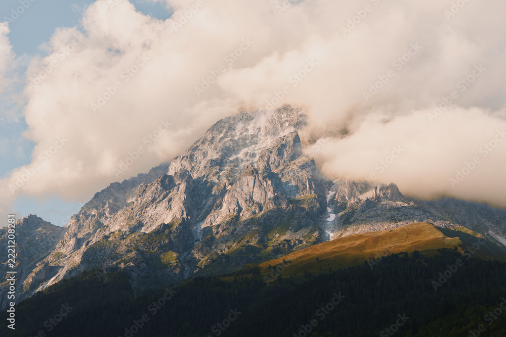 Fototapeta premium Majestic mountain peak rising above a pine forest, with wispy clouds, rugged rock, and expansive alpine landscape highlighting nature, scale, and solitude and calm mood.