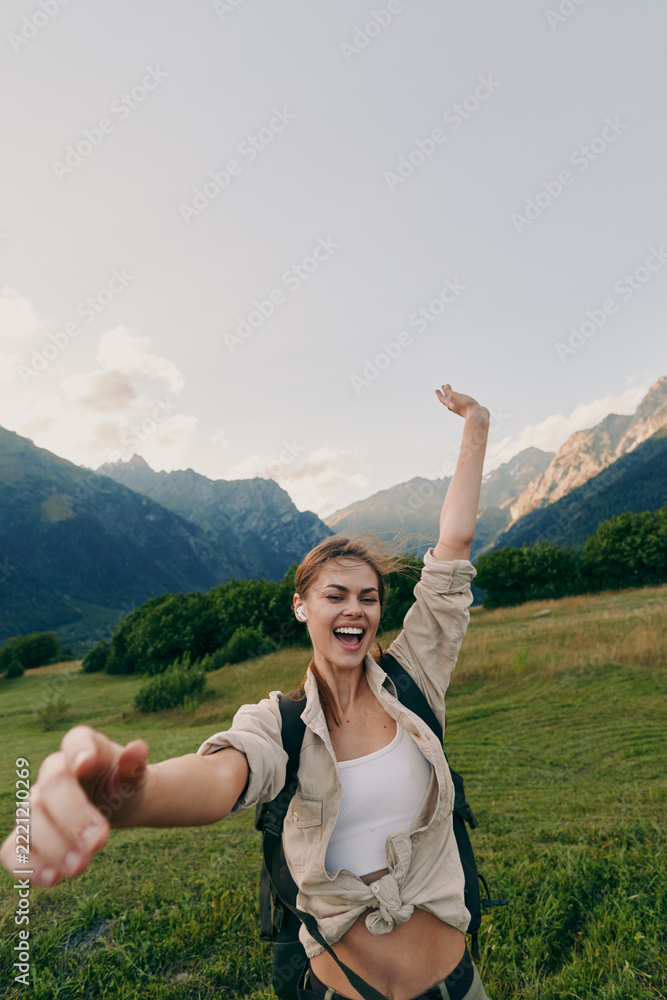 Fototapeta premium A joyful woman hikes through a green valley with distant mountains and a backpack, capturing a candid outdoors lifestyle moment of energy, freedom, and exploration.