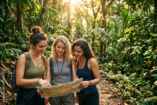 Three young women hiking with map in lush forest trail