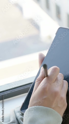 Vertical video: Stylus entering, right hand tapping tablet and noting at windowsill, copy space